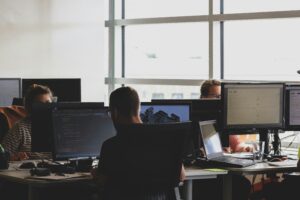 Technology professionals working at multiple computer monitors in a modern office, collaborating on software, digital projects, and business operations.