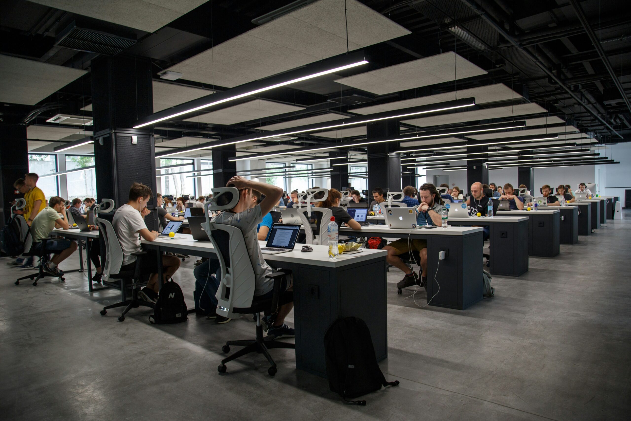 Technology professionals working on laptops and computers in a modern open office, showcasing collaboration, digital workspaces, and business productivity.