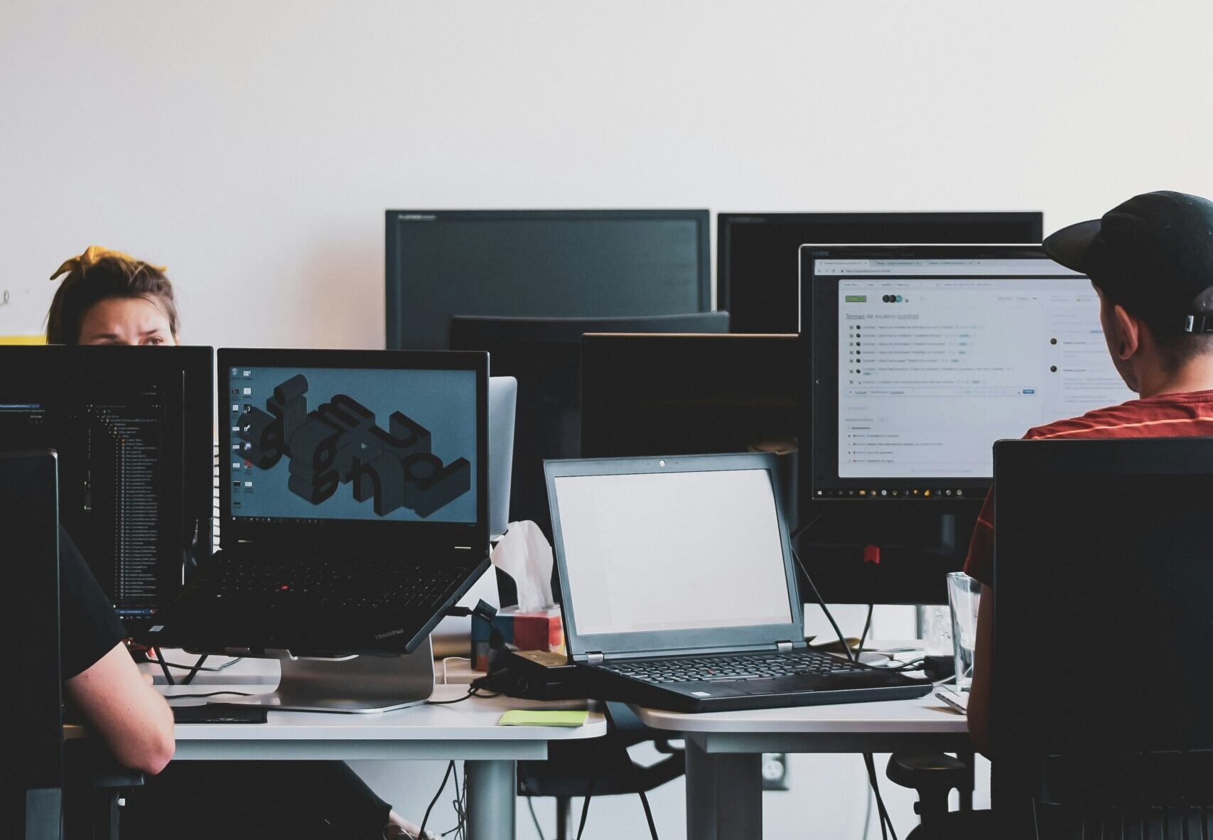 Software and technology professionals working at computer workstations in a modern office, with multiple monitors displaying development tools and business applications.