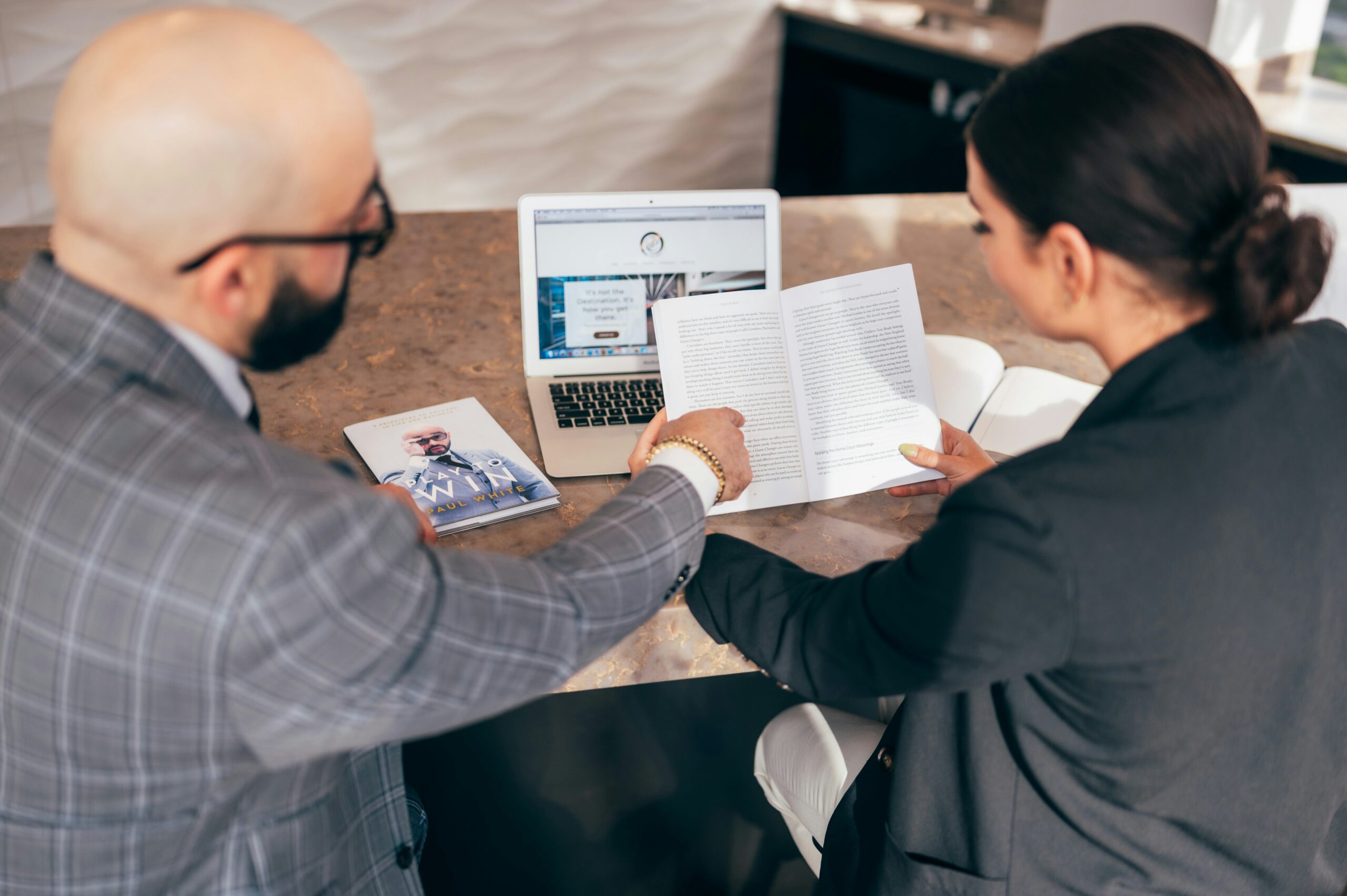 Business professionals reviewing documents and digital content on a laptop during a collaborative planning and research session.